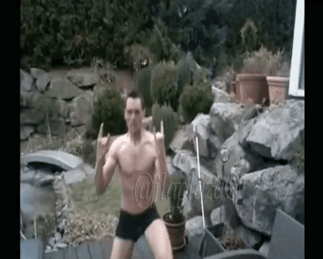 a man without a shirt is doing a rock and roll sign in front of a rock wall