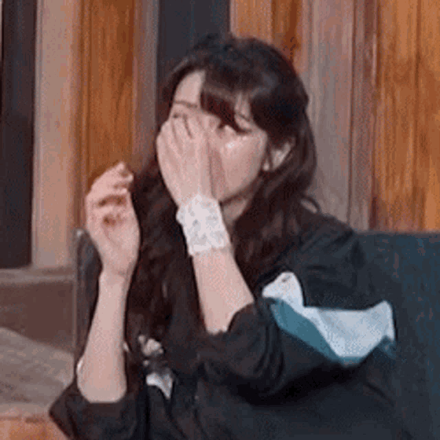a woman is sitting on a couch and covering her face with her hands .