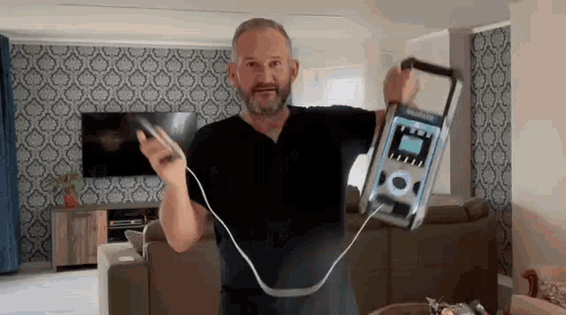 a man in a living room is holding a device that is plugged into a wall .