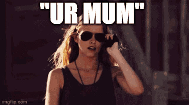 a woman wearing sunglasses is standing in front of a sign that says ur mum
