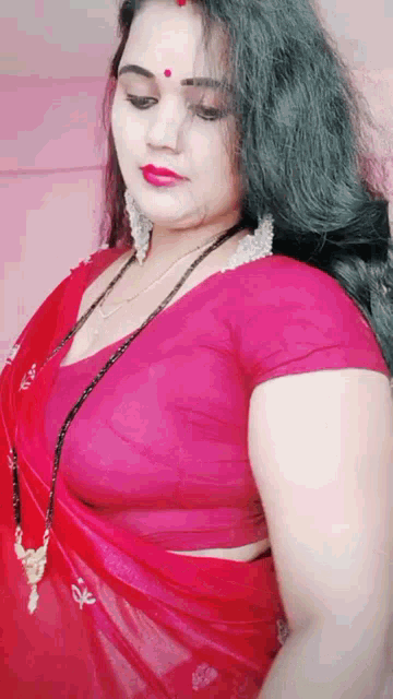 a woman in a red blouse and red saree is standing in front of a wall .