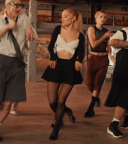 a woman in a crop top and skirt is dancing with a group of people