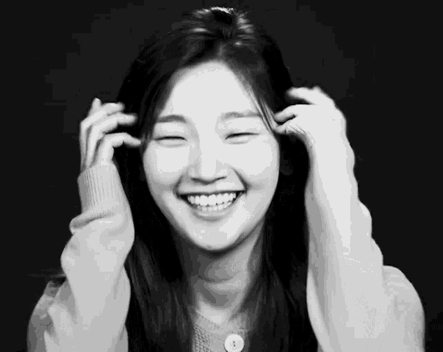 a woman is smiling with her eyes closed and her hands on her head .