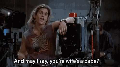 a man sitting in front of a camera with the words " and may i say you 're wife 's a babe "