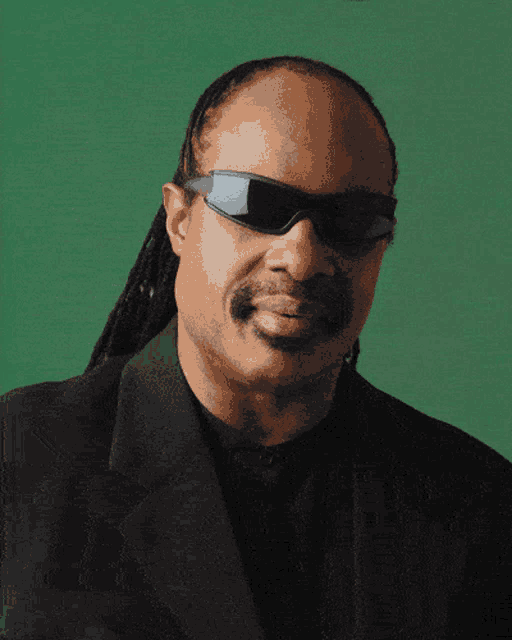 a man wearing sunglasses and a black suit is smiling