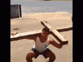 a man is squatting down carrying a wooden cross