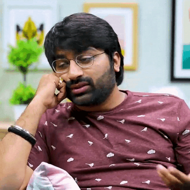 a man wearing glasses and a maroon shirt with birds on it is sitting on a couch