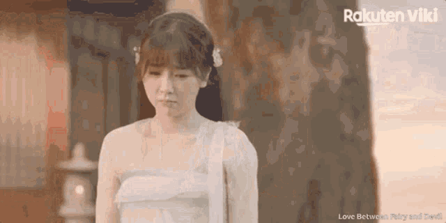 a woman in a white dress is standing in front of a tree and looking down .