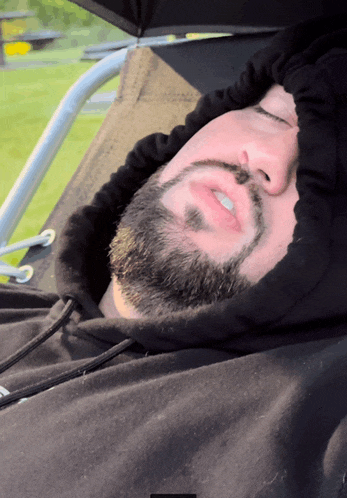 a man with a beard wearing a black hoodie is sleeping in a chair