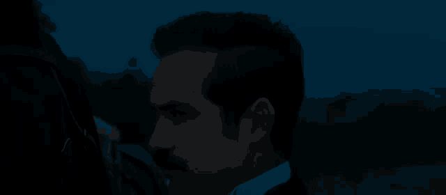 a man with a mustache is standing in the dark looking at something