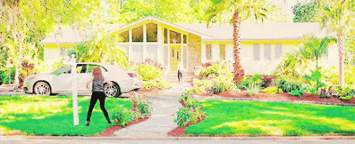 a woman is walking in front of a house with a car parked in front of it .