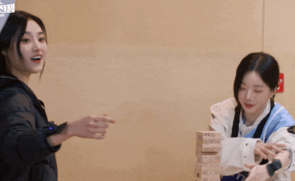 two women are playing a game with a stack of wooden blocks that says jenga on it