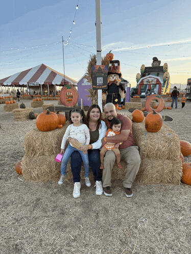 a family sits on a hay bale in a pumpkin patch