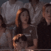 a group of people are sitting in a stadium watching a game and a woman is talking to a man .