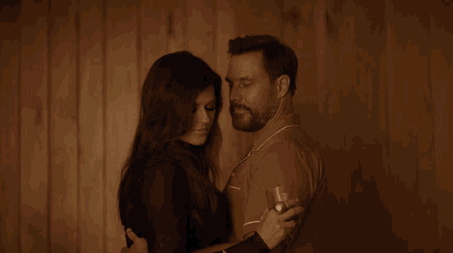 a man and a woman are hugging in front of a wood wall