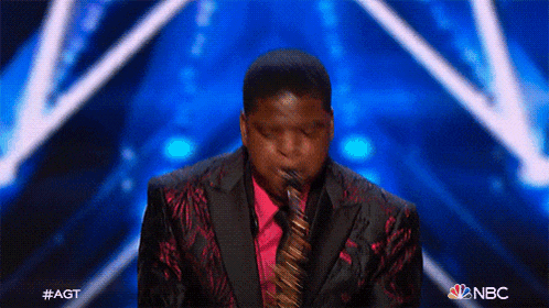 a man in a suit and tie is playing a saxophone on a stage with a nbc logo in the corner