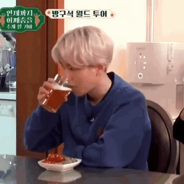 a man in a blue sweater is drinking a glass of beer while sitting at a table .