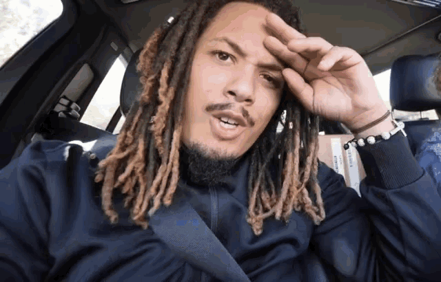 a man with dreadlocks is sitting in a car and covering his face
