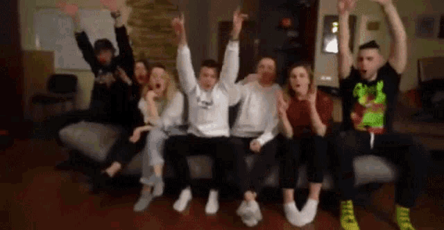 a group of people are sitting on a couch with their arms in the air and making funny faces .