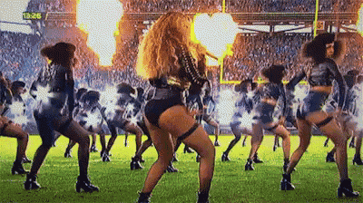 a group of cheerleaders are dancing on a field with fire coming out of the stands .