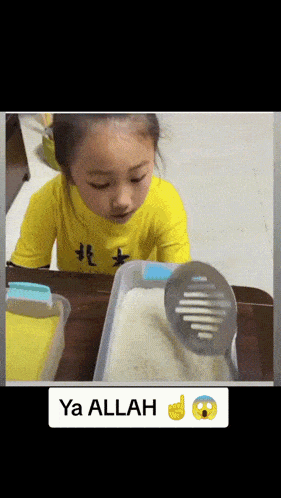 a little girl in a yellow shirt is playing with a spoon in a container of rice