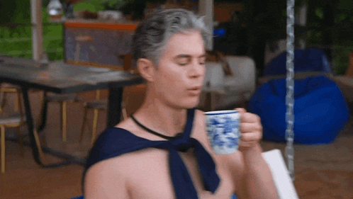 a shirtless man is drinking from a blue and white cup