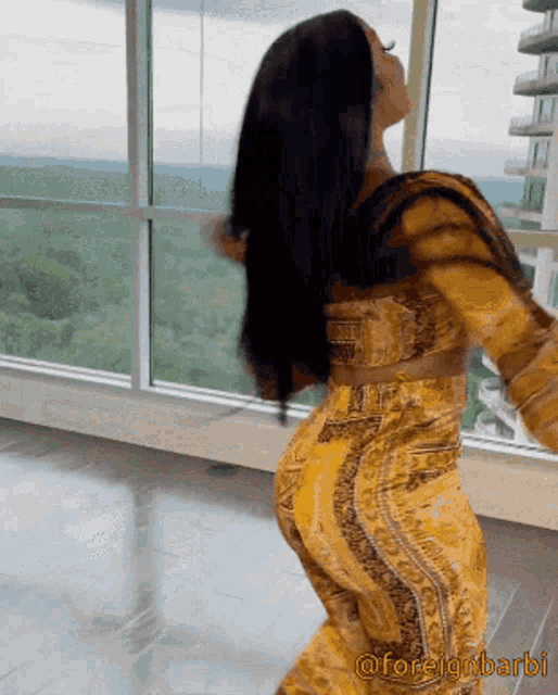 a woman in a yellow dress is dancing in front of a window with the caption @foreignbarbie