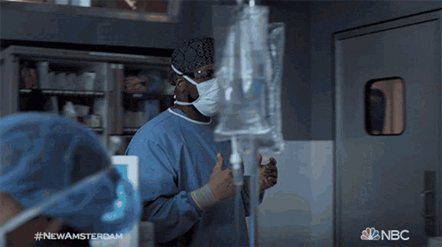 a surgeon wearing a mask and goggles is standing in front of a window with nbc written on the bottom