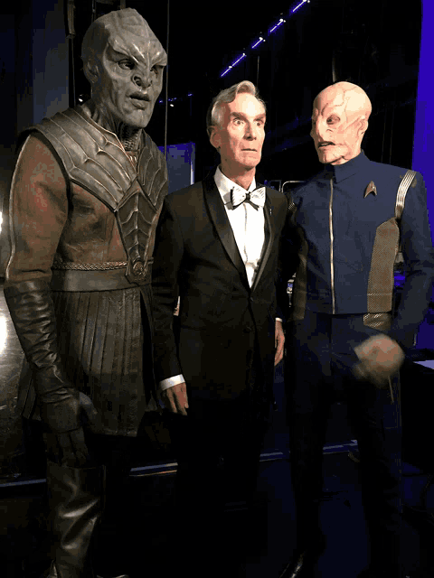 a man in a tuxedo and bow tie is standing next to two aliens