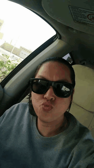 a woman wearing sunglasses and a gray shirt is sitting in a car