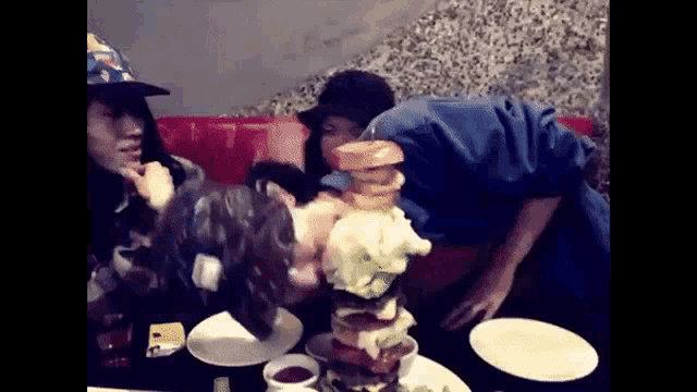 a group of people are sitting at a table with plates and a stack of hamburgers on it