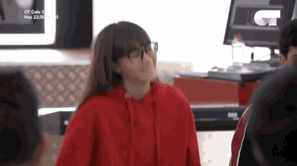 a woman wearing glasses and a red hoodie is standing in front of a computer monitor .