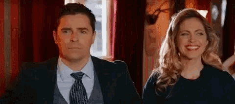 a man and a woman are standing next to each other in a room . the man is wearing a suit and tie .
