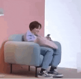 a person is sitting in a chair holding a pillow and looking at their phone .