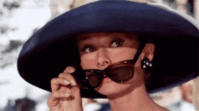 a woman wearing a blue hat and sunglasses is looking down .