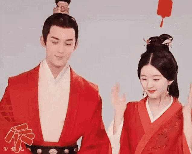 a man and a woman in traditional chinese clothing are standing next to each other and waving .