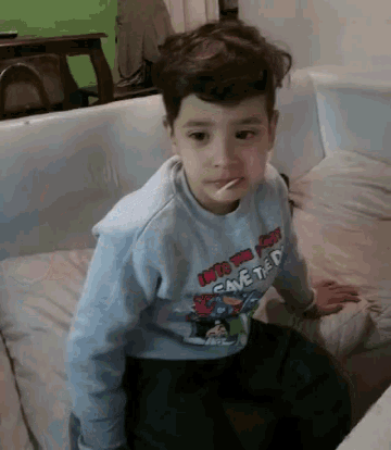 a young boy is sitting on a couch wearing a shirt that says " into the joker cave the "