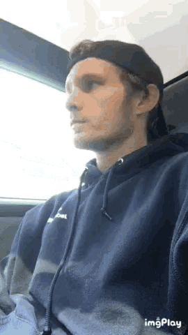 a man wearing a hat and a blue hoodie is sitting in a car .