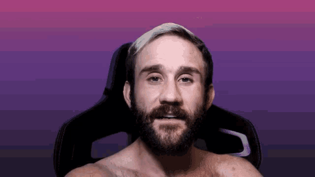 a shirtless man with a beard is sitting in a chair with a purple background
