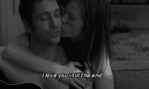 a black and white photo of a woman kissing a man on the cheek while holding a guitar .