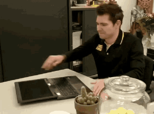 a man sitting at a table with a laptop and a jar of lemons in front of him