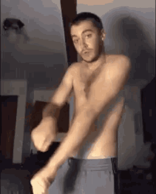 a shirtless man is dancing in a living room while wearing shorts .