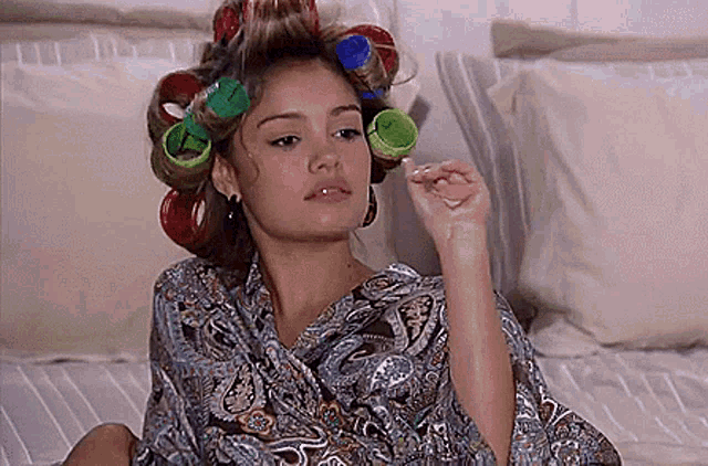 a woman with curlers in her hair is laying on a bed .