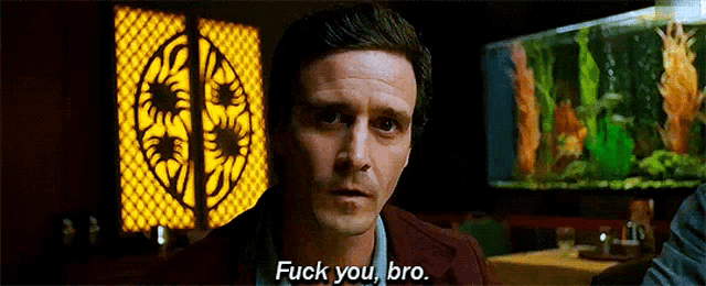 a man in a suit is talking to another man in front of an aquarium and says fuck you bro .