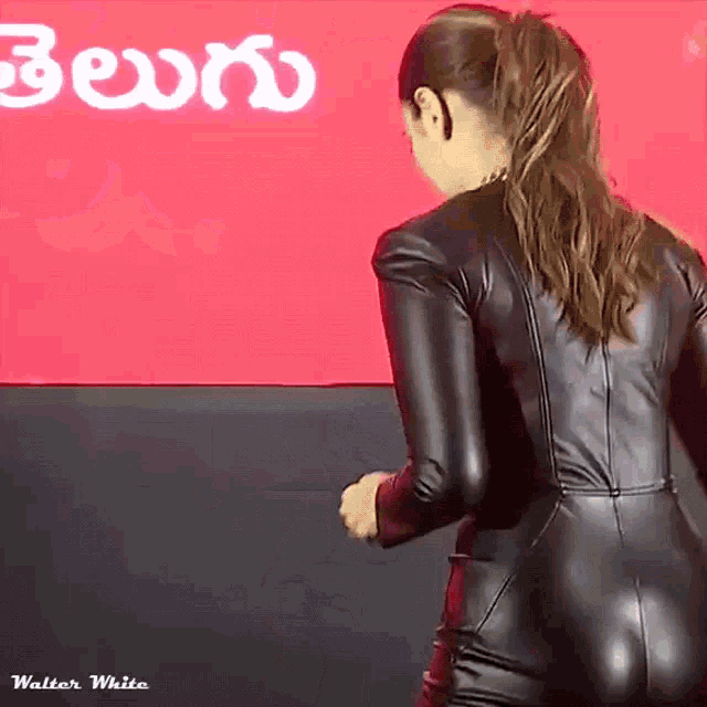 a woman in a black leather bodysuit is dancing in front of a red sign that says telugu