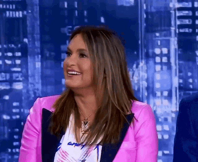 a woman in a pink jacket is smiling in front of a city skyline at night