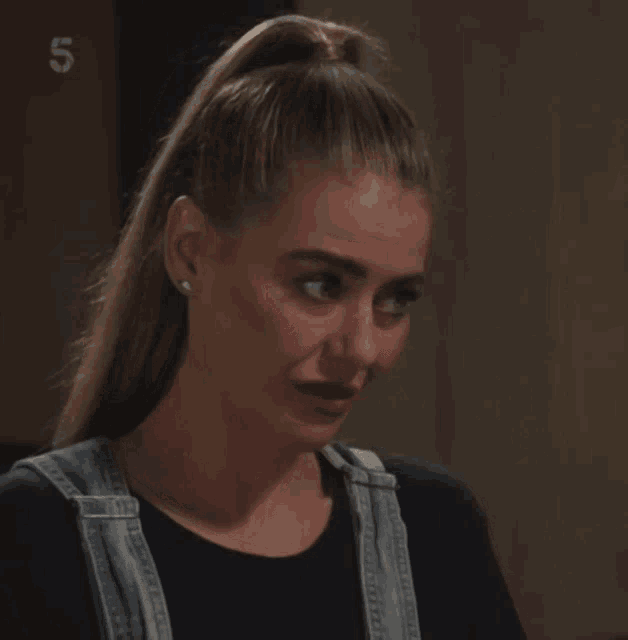 a woman wearing overalls and a black shirt looks down