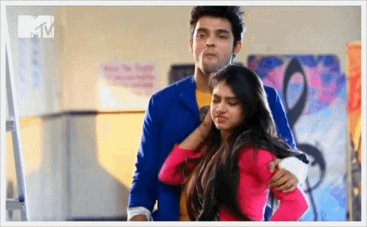 a man in a blue jacket is hugging a woman in a pink shirt with a mtv logo in the corner