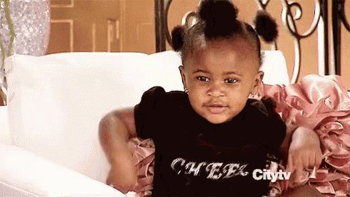 a little girl is sitting on a couch wearing a black shirt that says cheer .