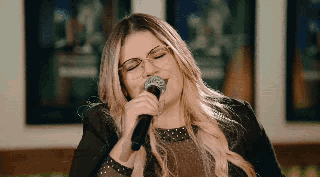 a woman with glasses singing into a microphone with her eyes closed